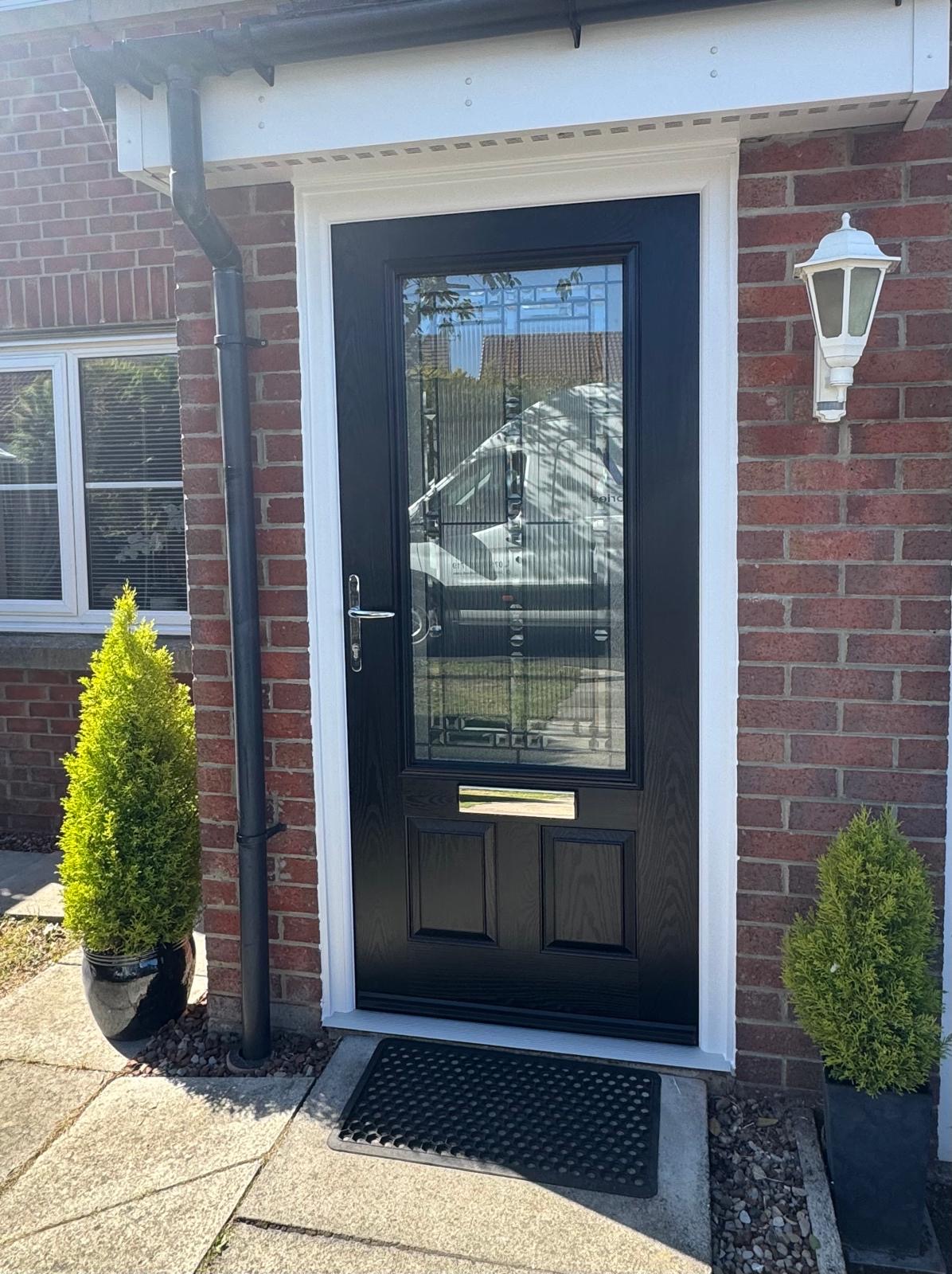 Black composite front door with a leaded glass panel, fitted into a brick house