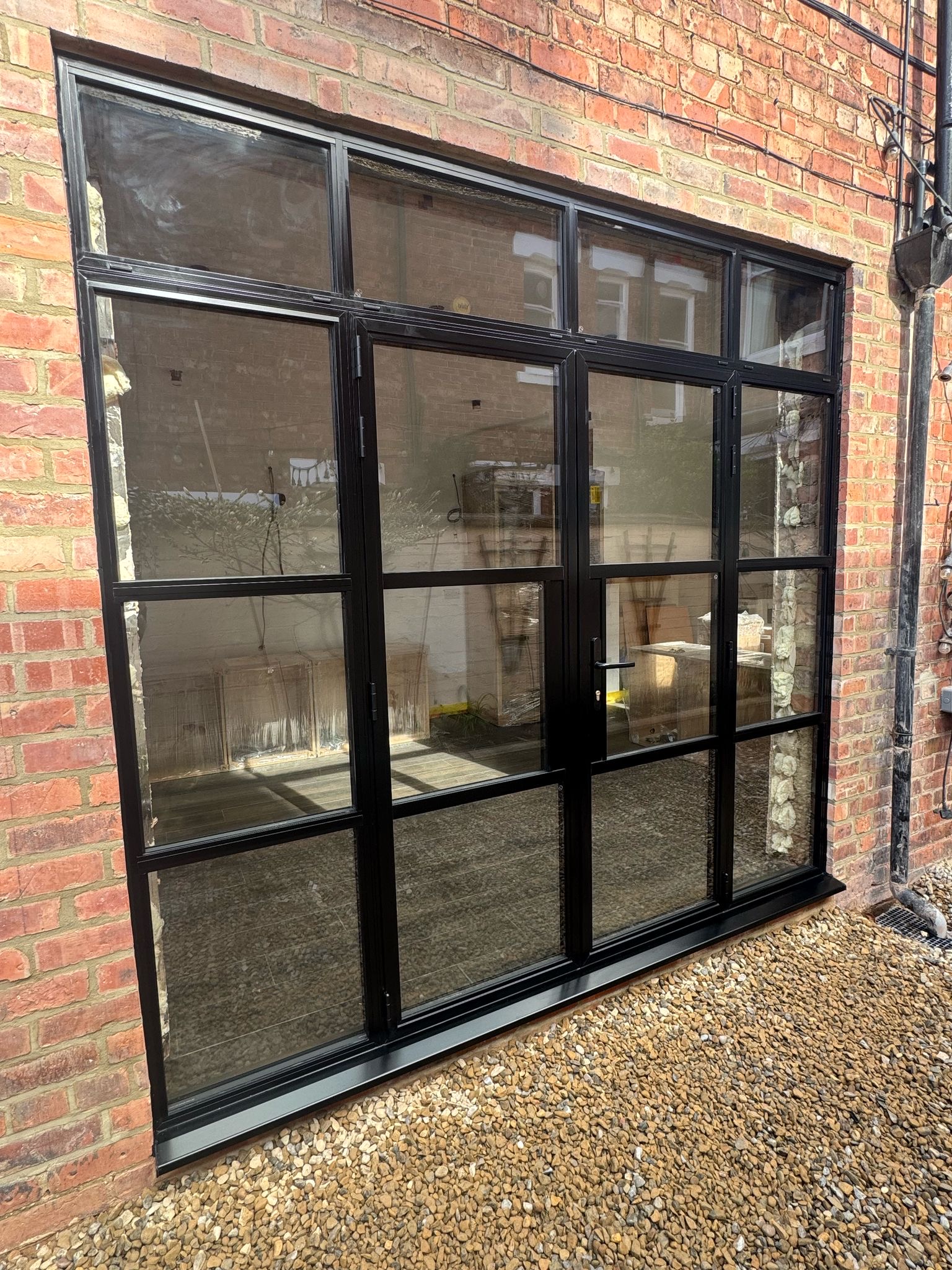 Black-framed glazed doors with grid bars set into a brick wall